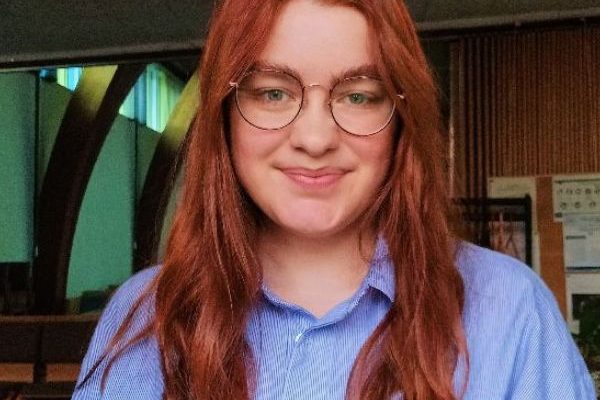 A photo of Alexandra, wearing a striped shirt, with red hair and round glasses.