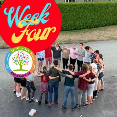 A group of children and youth standing in a circle on a gray concrete surface near a green hedge