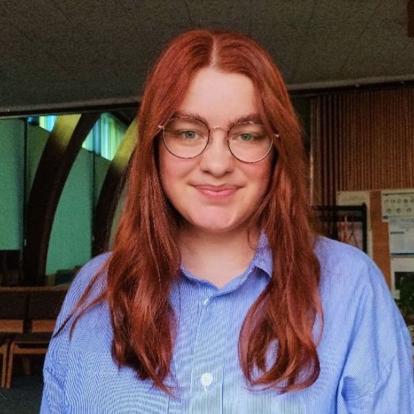 A photo of Alexandra, wearing a striped shirt, with red hair and round glasses.