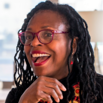 photo of a Black woman with locks, red framed eye glasses, and a huge smile